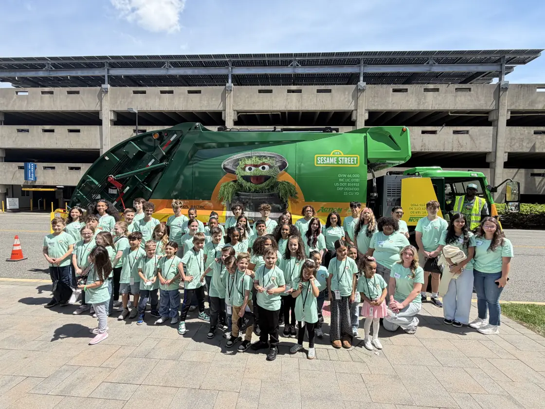 A large group of children in matching t-shirts posing in front of an Action Sesame Street collection truck on Bring Your Child to Work Day